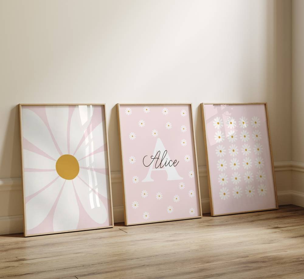 Trio d'affiche murale avec des illustrations de fleur marguerite. Le fond est rose pastelle. L'affiche du milieu comporte une initiale et prénom