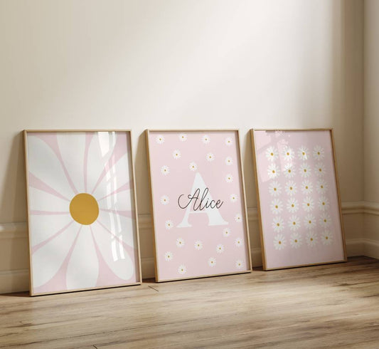 Trio d'affiche murale avec des illustrations de fleur marguerite. Le fond est rose pastelle. L'affiche du milieu comporte une initiale et prénom